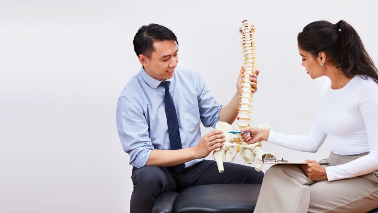 Male chiropractor and female chiropractor pointing at a human spine anatomy model