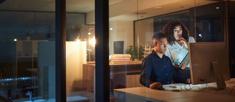 Two workers looking at a computer screen in an office at night