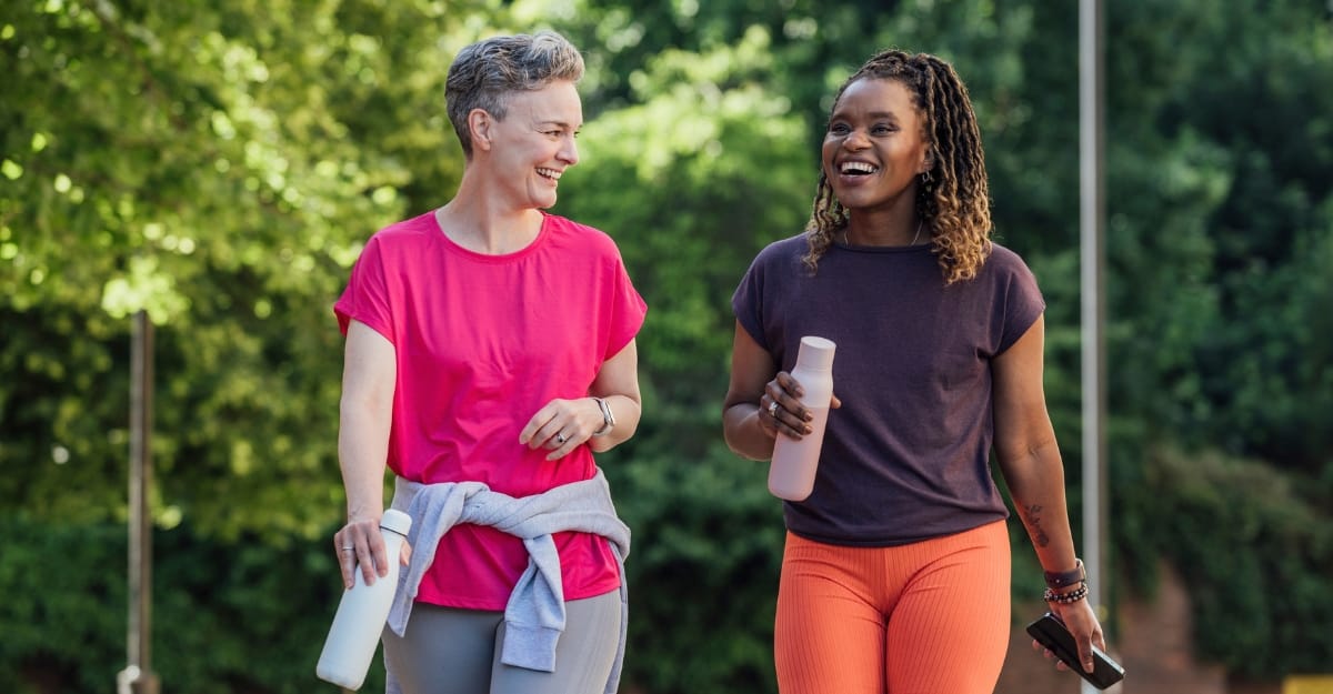 Two woman laugh while taking a walk in a park. (Photo: SolStock / iStock)